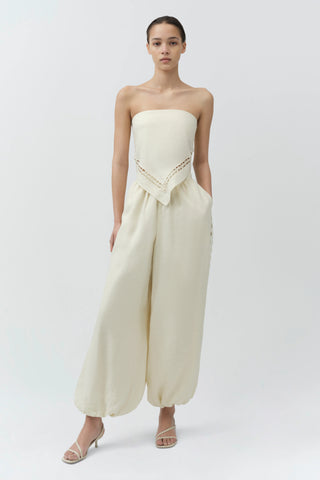 Woman wearing a strapless white jumpsuit with lace details on a white background