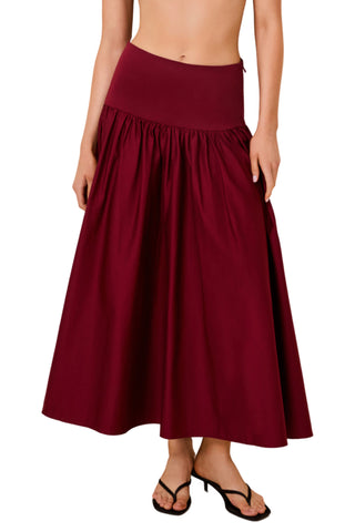 A woman wearing a high-waisted, flared midi skirt in deep burgundy with side pockets, paired with black thong sandals, shown against a plain white background.