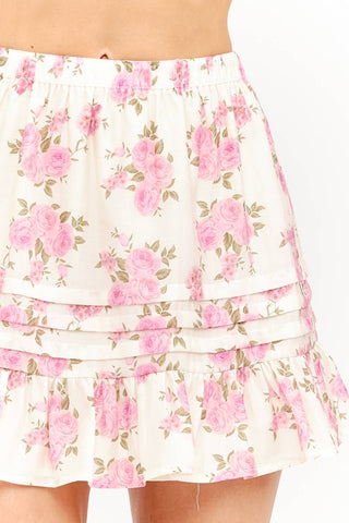 Model wearing a soft pink rose floral mini skirt with pleats and ruffled tiers on a white background
