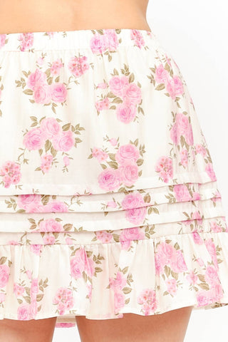 Model wearing a soft pink rose floral mini skirt with pleats and ruffled tiers on a white background