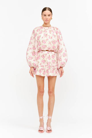 Model wearing a soft pink rose floral mini skirt with pleats and ruffled tiers on a white background