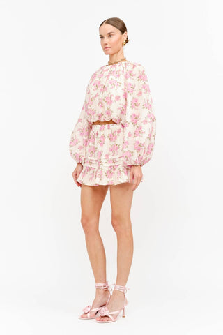 Model wearing a soft pink floral long sleeve blouse with a billowy silhouette, gathered neckline, and elasticized cuffs