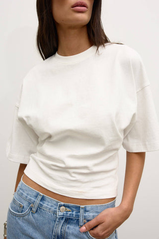 Person wearing a white cropped sweater and blue jeans against a plain background