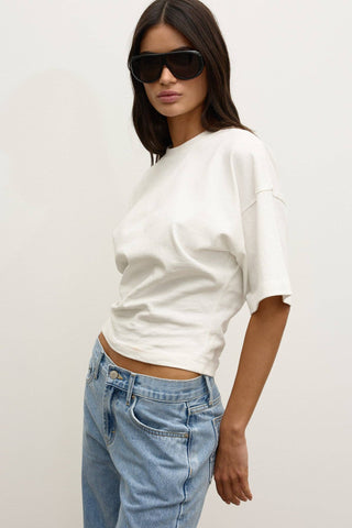 Woman wearing a white oversized shirt and light blue jeans with sunglasses on a plain background