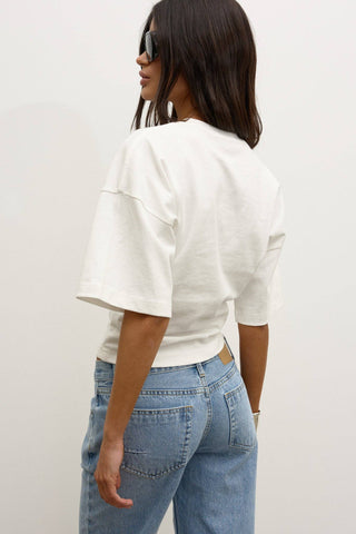 Person wearing a white top and blue jeans against a plain background