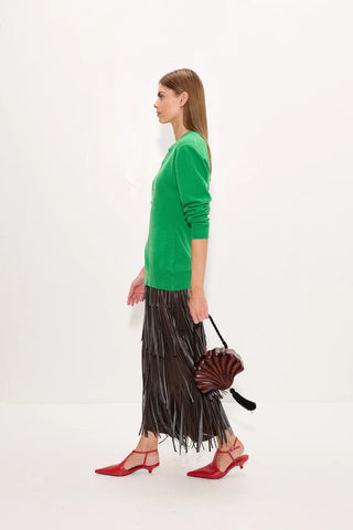 Woman wearing a green sweater and black pleated skirt with red shoes on a white background