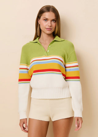 Woman wearing a green sweater with colorful stripes and beige shorts against a beige background
