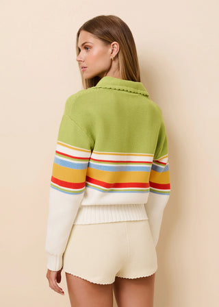 Woman wearing a green sweater with colorful stripes and white shorts against a beige background