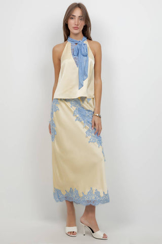 Woman wearing a cream-colored dress with blue lace details against a white background