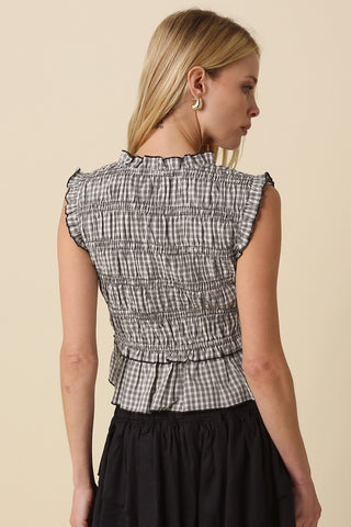 Woman wearing a gingham lace up smocked top with ruffle cap sleeves and a subtle peplum hem
