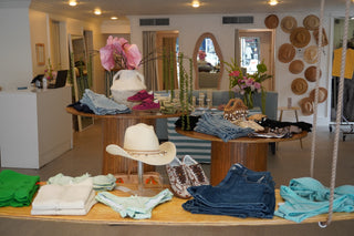 Display of clothing and accessories in a store with hats and jeans on tables.