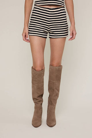Person wearing striped shorts and brown knee-high boots on a plain background