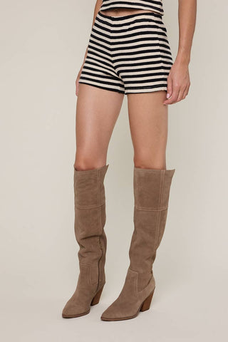 Person wearing black and white striped shorts with brown knee-high boots on a beige background