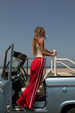 Woman in a red outfit standing next to an open car on a beach.