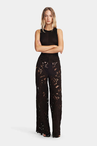 Woman wearing a black sleeveless top and black pants with cut-out details on a white background