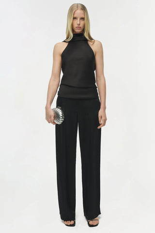 Woman wearing a black sleeveless top and pants holding a silver clutch on a white background