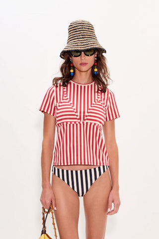 Woman wearing a red and white striped top and black and white striped shorts with a hat and sunglasses on a white background.