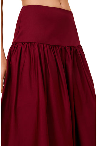 A close-up of a dark red or burgundy skirt with a wide waistband and gathered, flowing fabric, shown on a model against a plain white background.