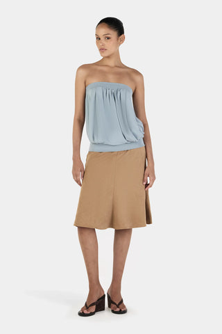 Woman wearing a light blue strapless top and beige skirt on a white background