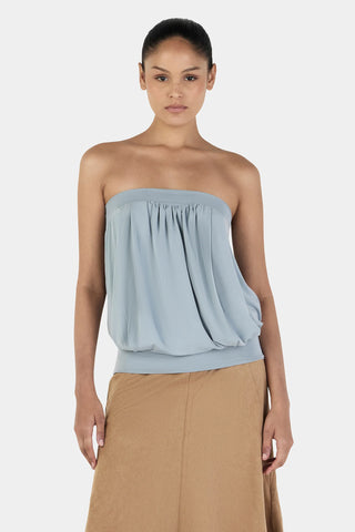 Woman wearing a light blue strapless top and beige skirt on a white background