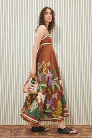 Woman wearing a brown floral dress holding a handbag against a striped wall.