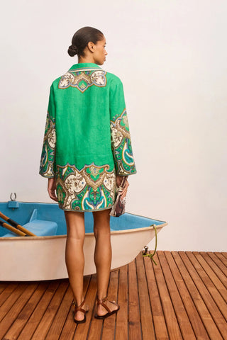 Woman in a green embroidered dress standing on a wooden deck with a small boat.
