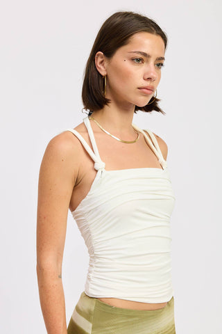 Woman wearing a white tank top with thin straps against a plain background
