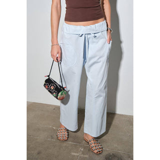 Person wearing light blue pants and a brown top, holding a black clutch with floral design.