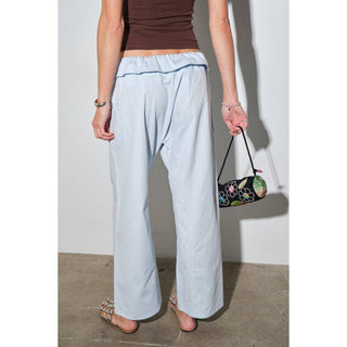 Person wearing light blue pants and a brown top, holding a colorful handbag against a plain background.