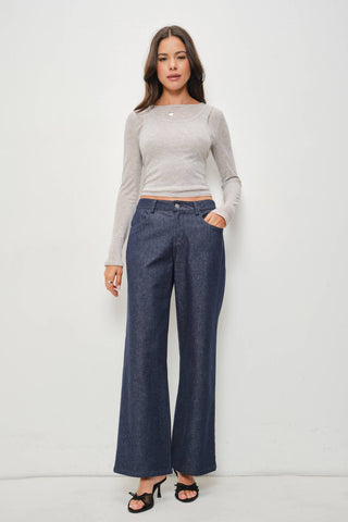 A woman modeling a light gray long-sleeve knit crop top and dark blue wide-leg denim pants against a plain white studio background.