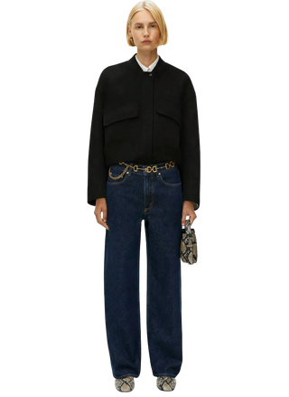 Person wearing a black jacket and blue jeans with a white background