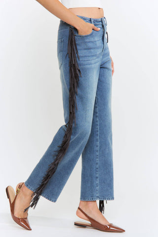 Blue jeans with fringe details worn by a person on a white background