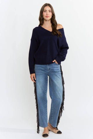 Woman wearing a navy sweater with a fringe detail on a white background