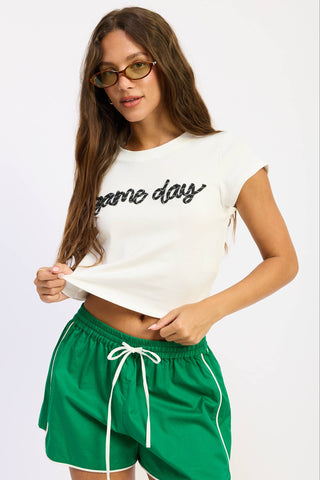 Woman wearing a white 'game day' shirt and green shorts on a white background
