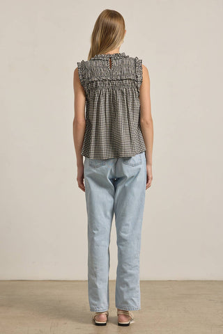 Woman wearing a checkered sleeveless top and light blue jeans against a plain background