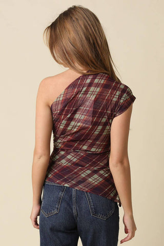 A woman shown from the back wearing a one-shoulder plaid top in burgundy, green, and beige tones, paired with blue jeans, against a solid beige background.