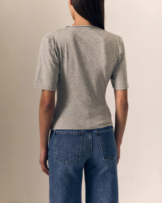 A woman shown from the back wearing a heather gray short-sleeve t-shirt and blue jeans, standing against a plain beige studio background.