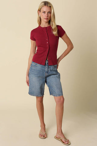 Woman wearing a red shirt and blue denim shorts on a beige background