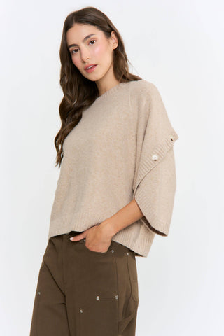 Woman wearing a beige poncho over a brown outfit on a white background