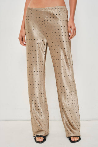 A person wearing shiny beige wide-leg pants with a small black polka dot pattern, paired with black slide sandals, shown against a plain light background.