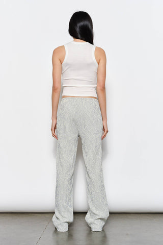 Person wearing a white sleeveless top and light gray pants against a white background