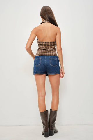 Woman wearing a plaid top and denim shorts with brown boots on a white background