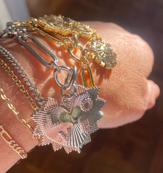 Close-up of a hand wearing multiple gold and silver bracelets with detailed charms.