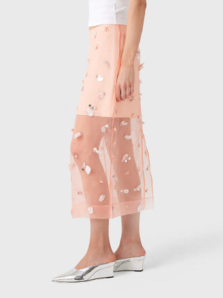 Woman wearing a sheer pink skirt with floral embroidery on a white background