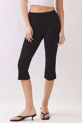 A model wearing black capri pants with side seam detailing, paired with black thong sandals and a white crop top, shown against a plain light gray studio background.
