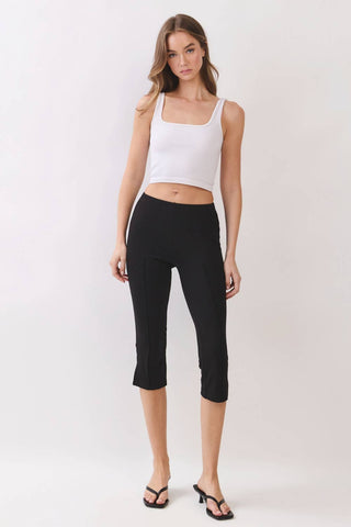 A woman modeling a white cropped tank top and black cropped capri pants against a plain light gray studio background.