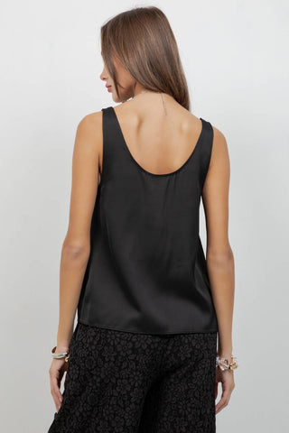 Woman wearing a black sleeveless top and black patterned pants on a light gray background