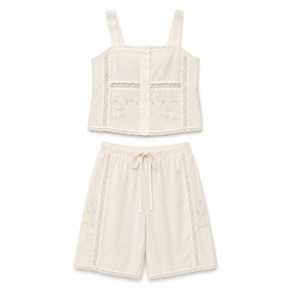A two-piece baby loungewear set in cream cotton, featuring a sleeveless button-front crop top with floral embroidery and lace trim, and matching drawstring shorts with lace side panels and floral embroidery.