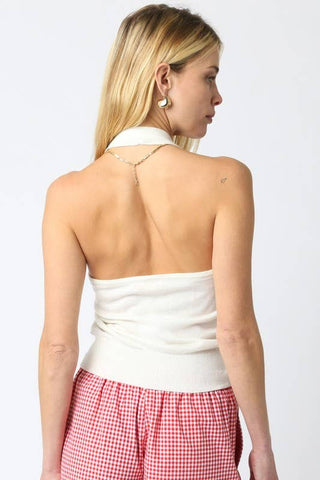 Woman wearing a white top with an open back and red checkered pants on a plain background