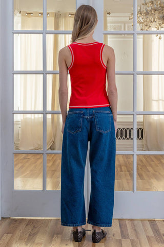 Person wearing a red tank top and blue jeans standing in front of a glass door.